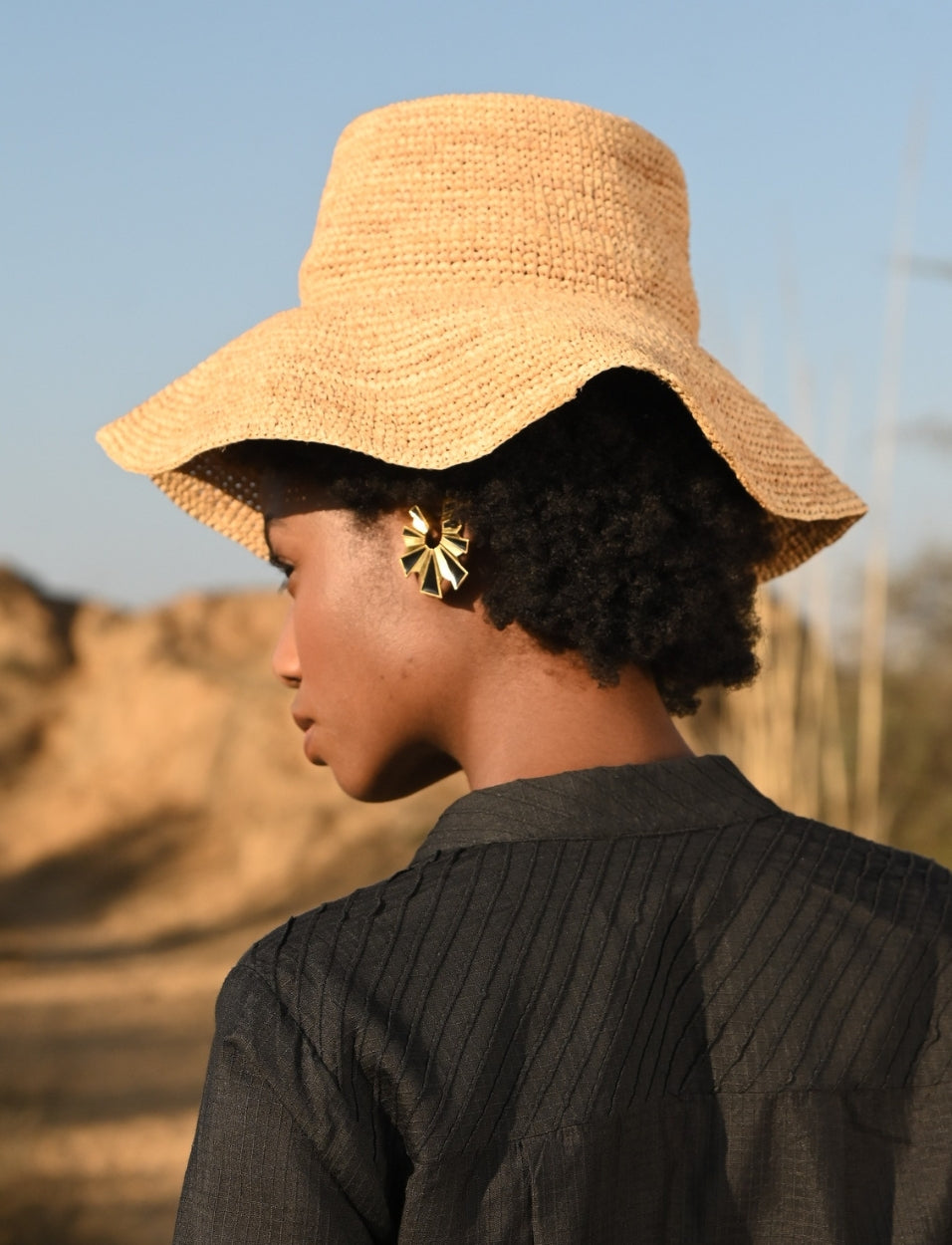 Woman wearing a wide-brimmed straw hat and gold geometric earrings in an outdoor setting
