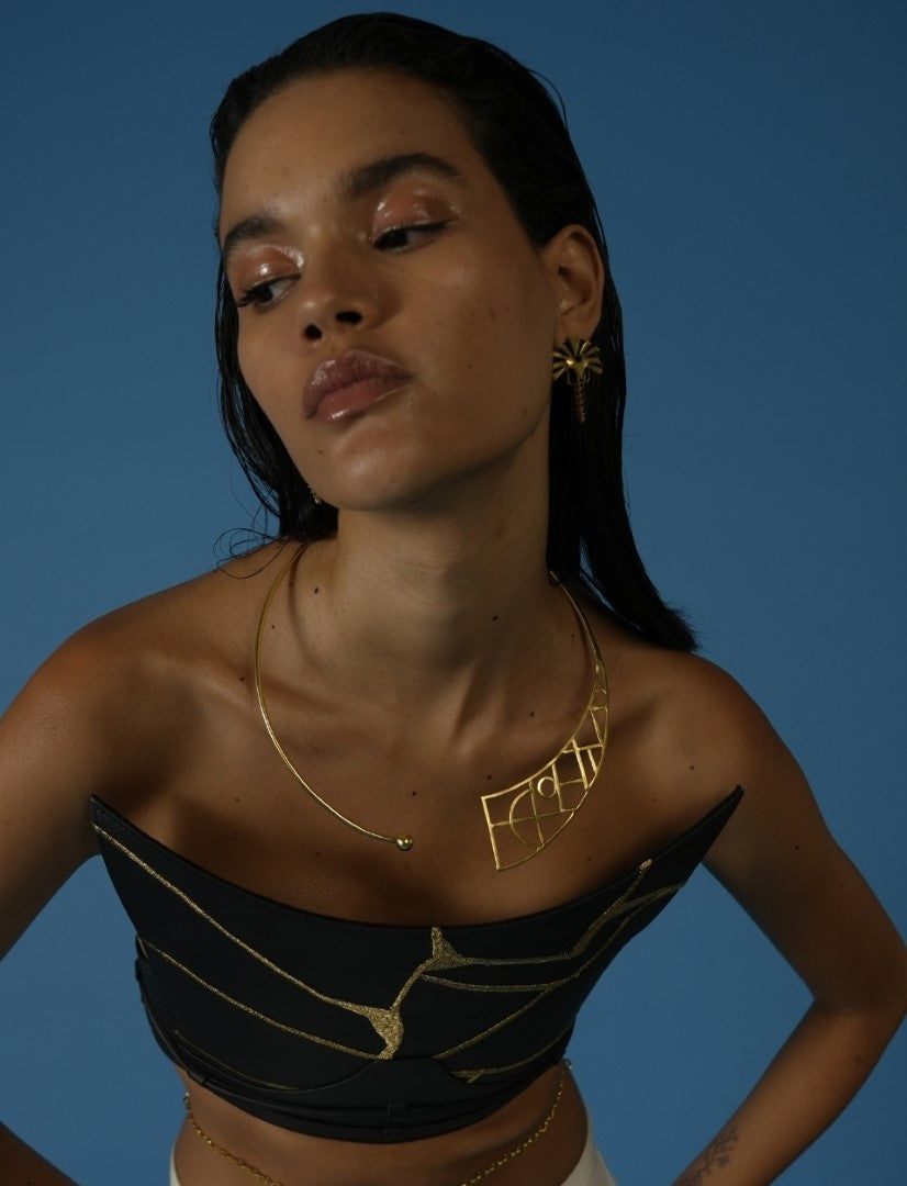 Woman wearing a sculptural metal wire choker with geometric design and matching gold earrings against blue background