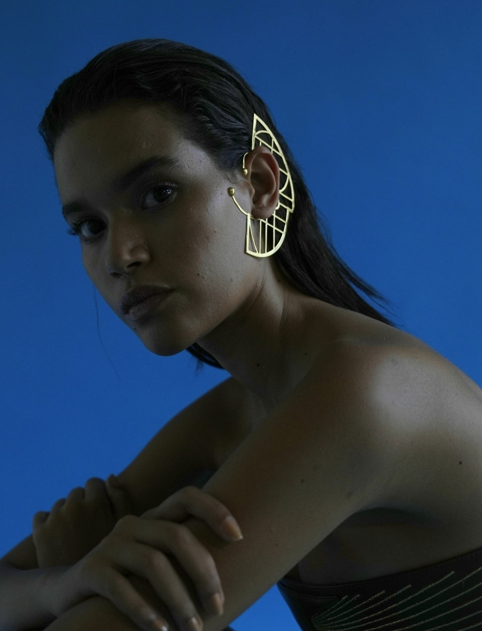 Model wearing an adjustable gold metal ear cuff with geometric design against a blue background
