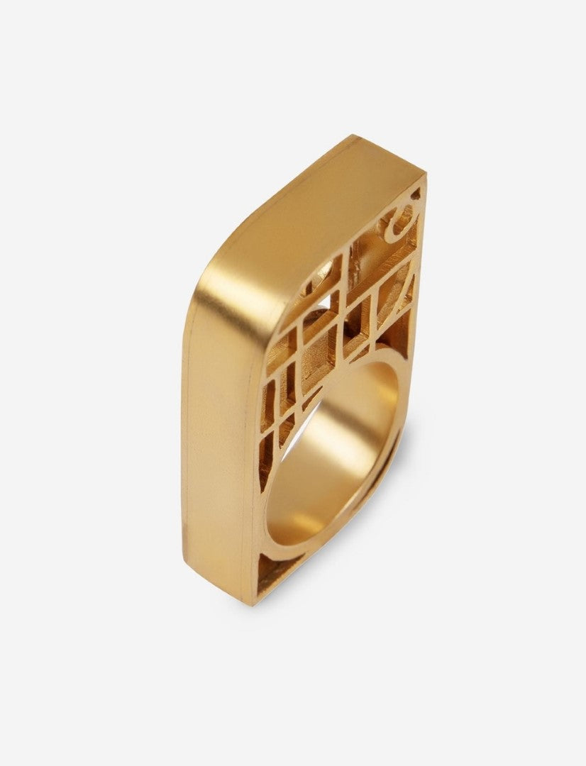 Gold-toned metal ring with a square top featuring a cutout geometric pattern on a white background
