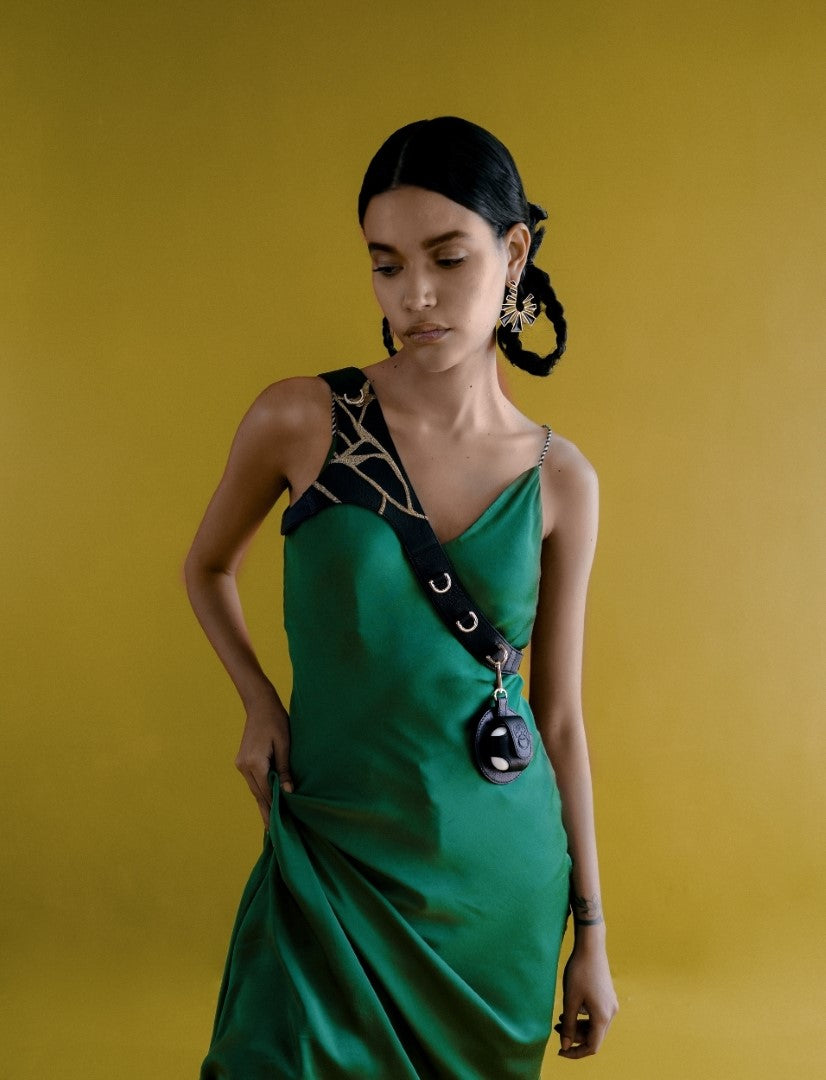 Woman in green satin dress with black strap and artistic gold earrings against yellow background