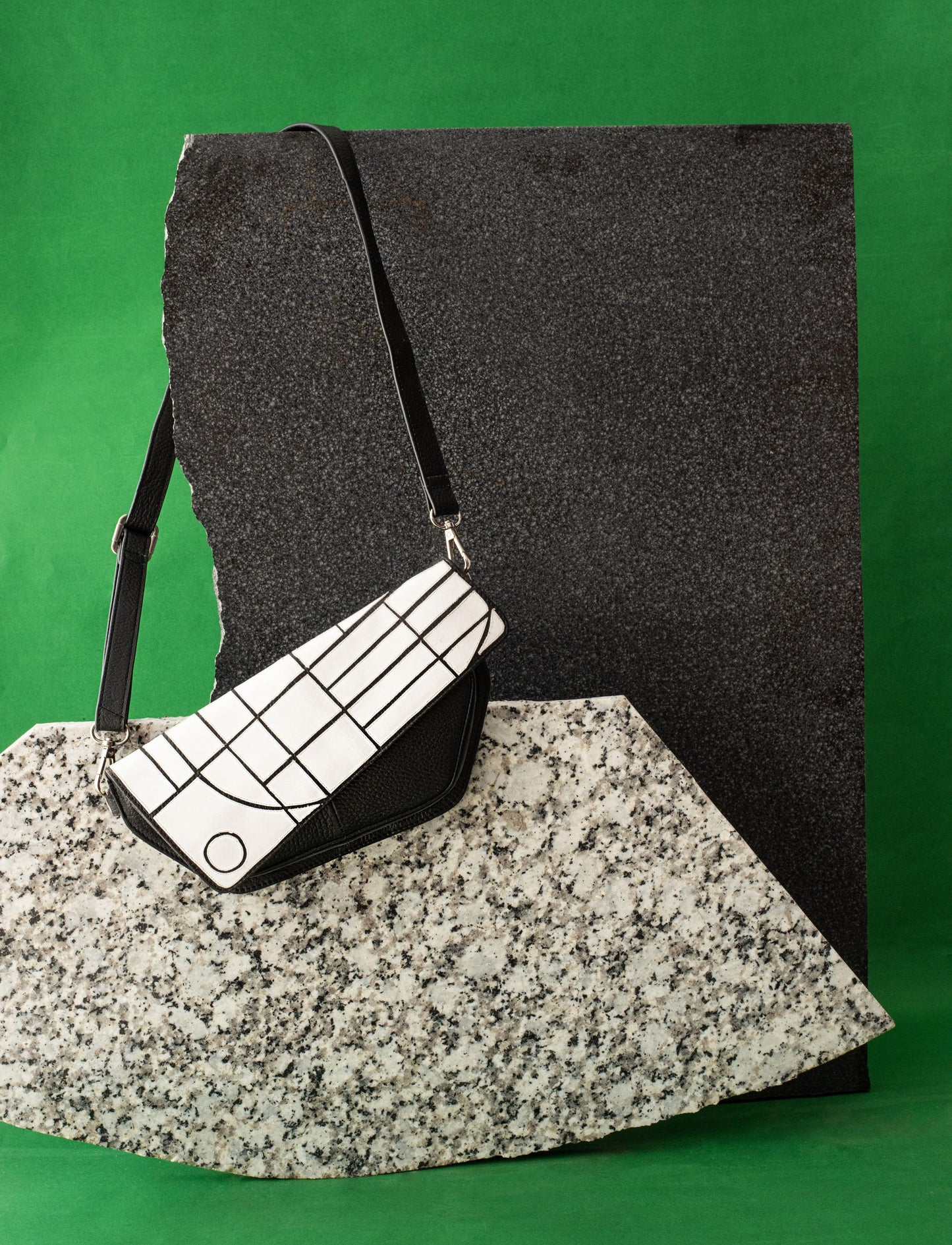 Black and white geometric patterned handbag with black strap on textured stone slabs against green background