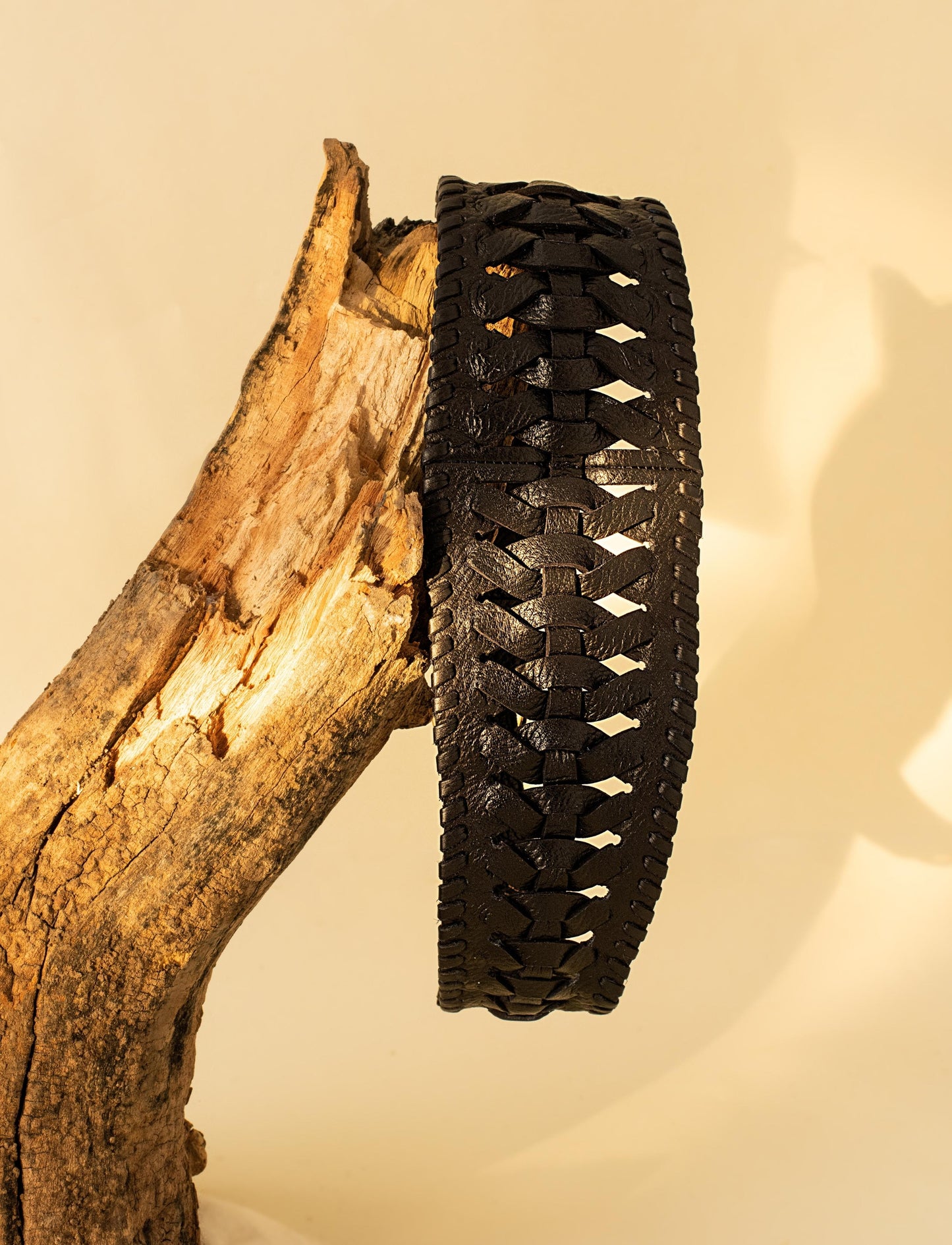 Black woven leather bracelet displayed on a textured tree branch against beige background