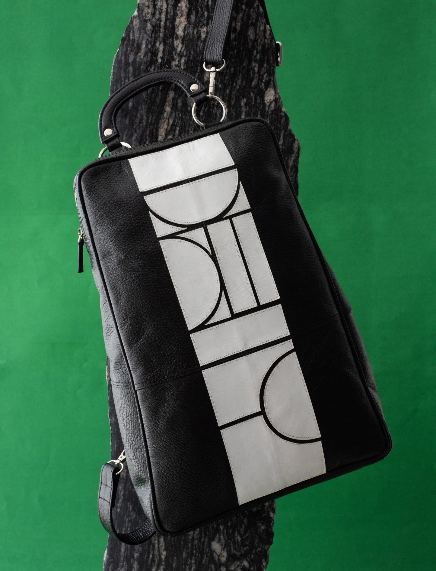 Black leather backpack with white abstract geometric pattern on textured black and green background