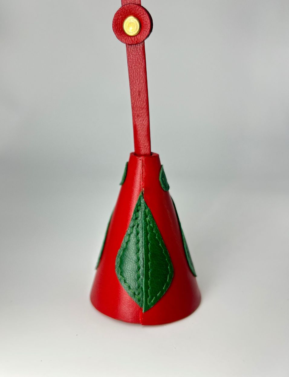 Red leather bell-shaped charm with green leaf applique and gold button on strap