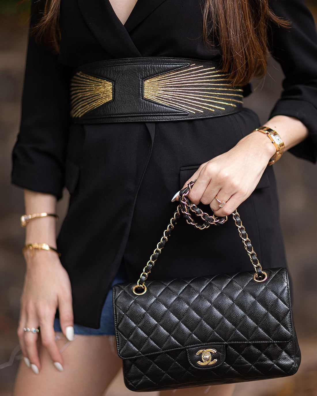 Woman in black blazer with wide belt holding black quilted Chanel handbag with gold chain strap
