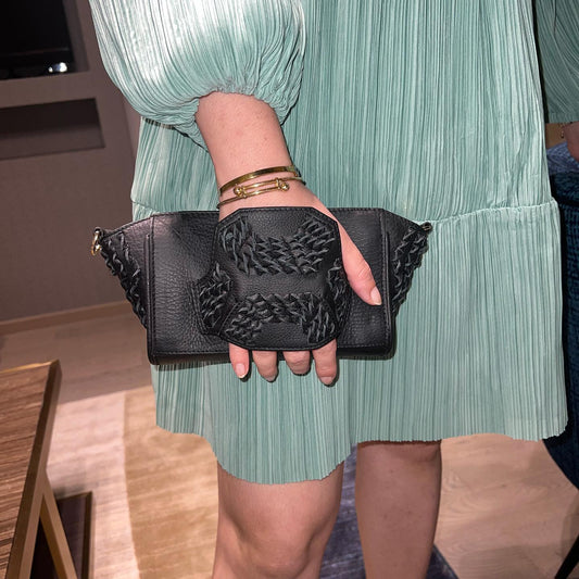 Woman in pleated mint green dress holding black leather clutch with braided details and gold bracelets