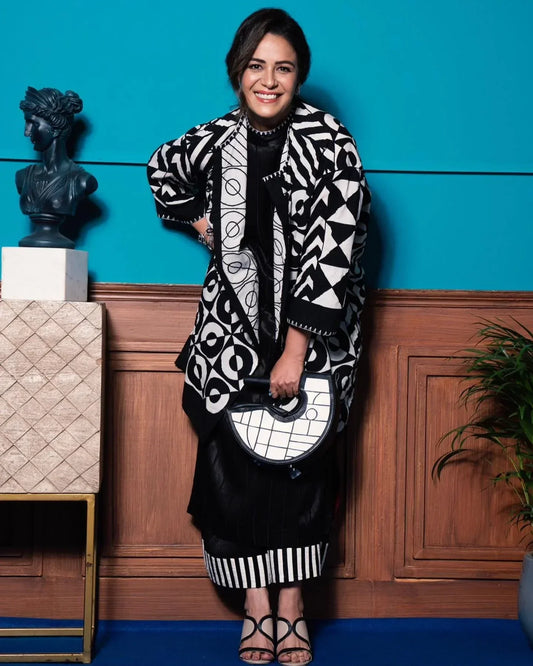 Smiling woman in black and white geometric patterned outfit holding matching half-circle handbag, blue background