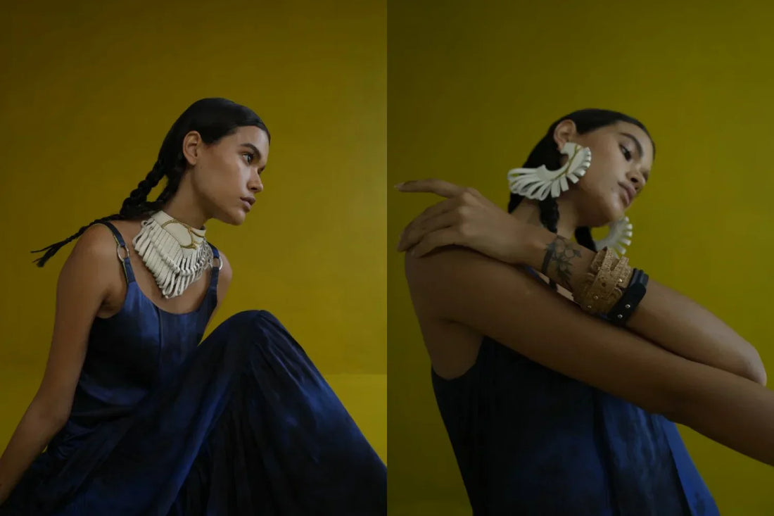 Woman in blue dress with braided hair wearing bold white jewelry against mustard yellow background