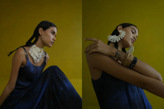 Woman in blue dress with braided hair wearing bold white jewelry against mustard yellow background