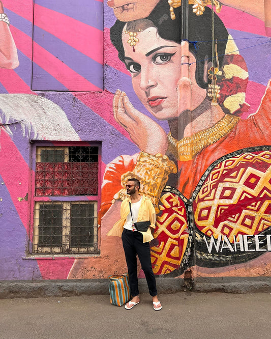 Man in yellow shirt and sunglasses standing against vibrant mural of traditional Indian dancer in bold colors