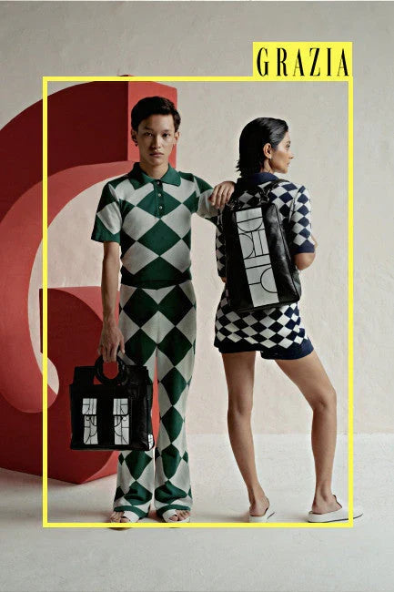 Two models in green and blue harlequin pattern outfits posing with black designer bags against minimalist backdrop