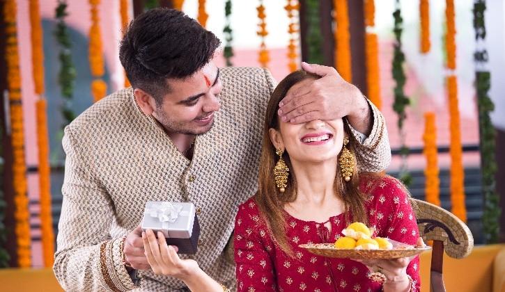 Happy Indian couple celebrating festival with traditional sweets and gift in decorated setting