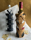 Two bottles, one wine and one clear, in stylish cork and black leather upcycled stitched wine cases on white surface with vintage playing cards