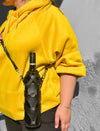 Person wearing bright yellow hoodie carrying black leather upcycled stitched wine bottle case with adjustable strap