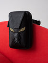 Black textured leather belt bag with gold embroidered detail resembling a face on red background