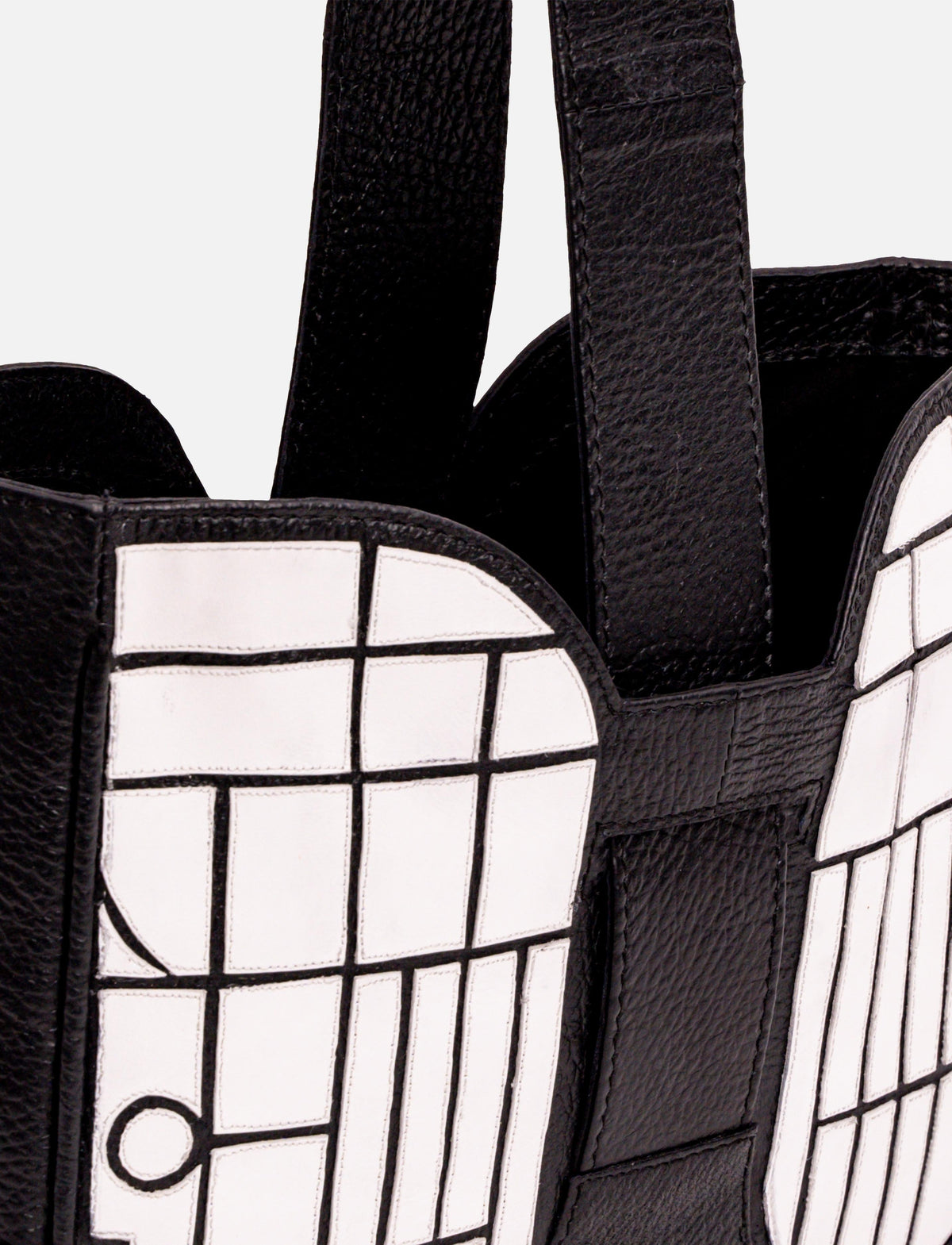 Close-up of black leather bag with white grid pattern and wide straps