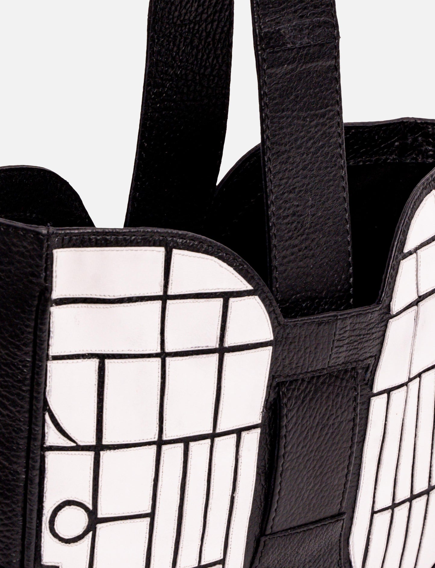 Close-up of black leather bag with white grid pattern and wide straps