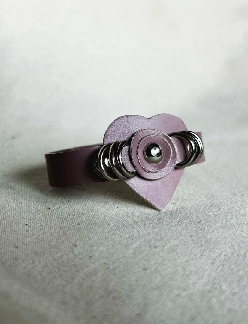 Pink vegan leather cuff bracelet with silver ring studs and heart-shaped centerpiece on fabric surface