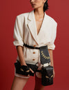 Woman wearing oversized white blazer with gold buttons and black leather accessories with gold embroidery against red background