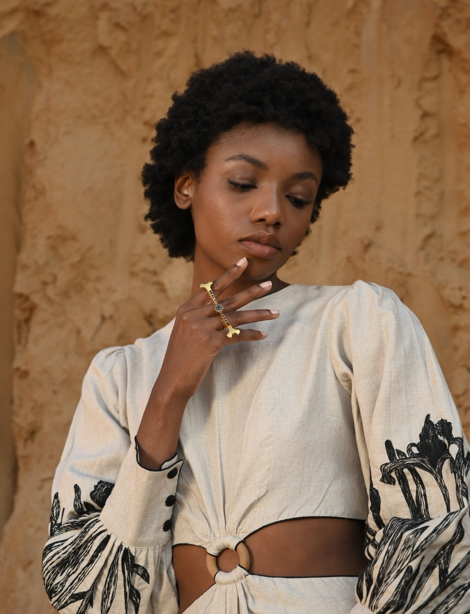 Woman with natural afro hairstyle wearing beige dress with black floral embroidery and gold finger ring