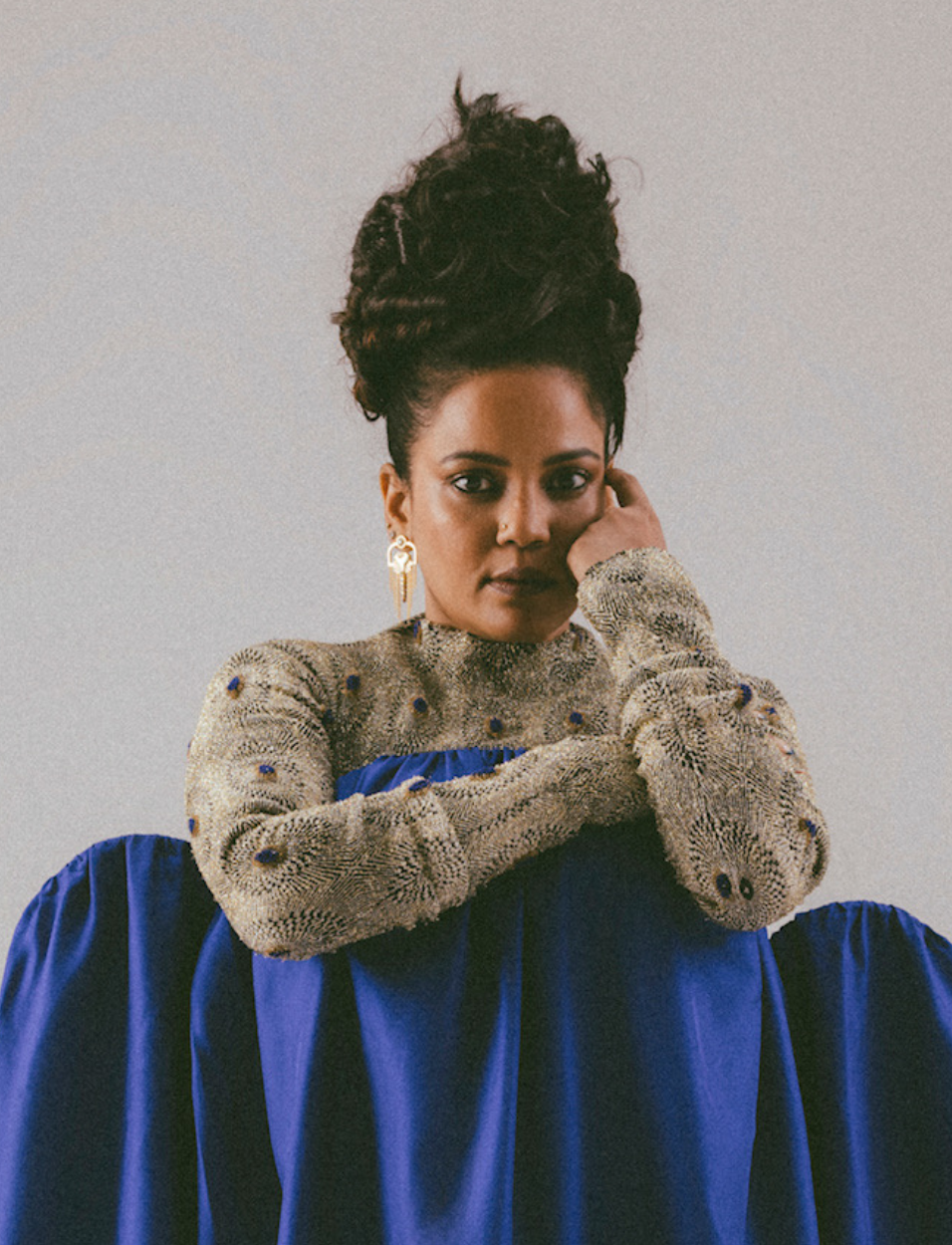 Portrait of a woman with curly updo wearing a textured beige top with blue accents and a flowing blue skirt
