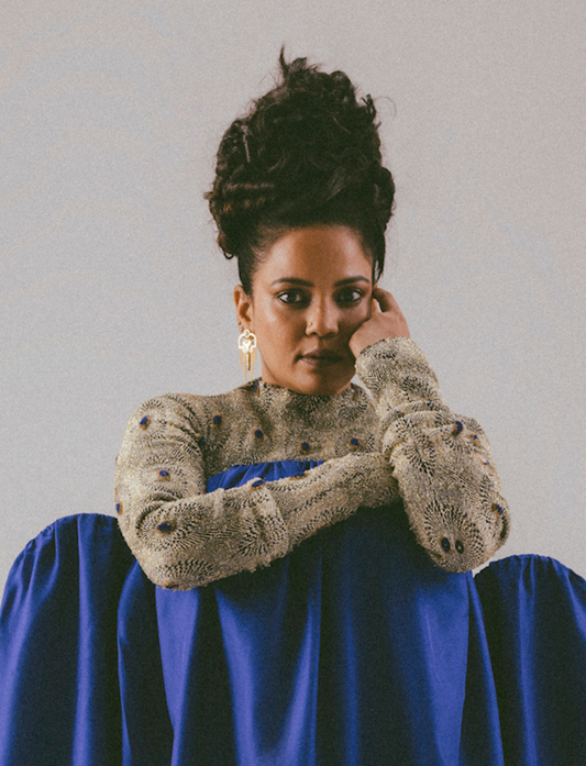 Portrait of a woman with curly updo wearing a textured beige top with blue accents and a flowing blue skirt