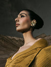 Woman in textured mustard garment wearing geometric gold earrings with desert mountains background