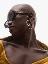 Close-up of stylish bald woman wearing black sunglasses, gold spiral hoop earring, and mustard yellow top