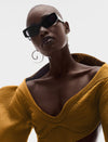 Fashion model wearing mustard yellow textured top, black sunglasses, and large gold hoop earrings