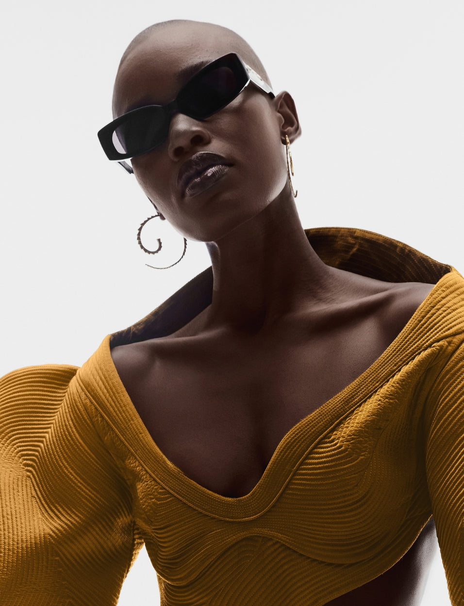 Fashion model wearing mustard yellow textured top, black sunglasses, and large gold hoop earrings
