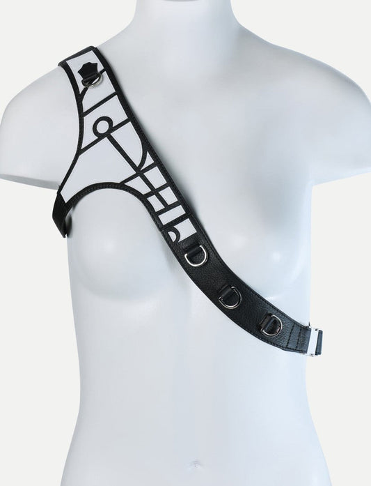Black leather one-shoulder harness with metal D-rings and geometric applique on mannequin bust