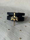 Timeless black leather wrap bracelet with gold lion head pendant on light fabric surface with small gold beads