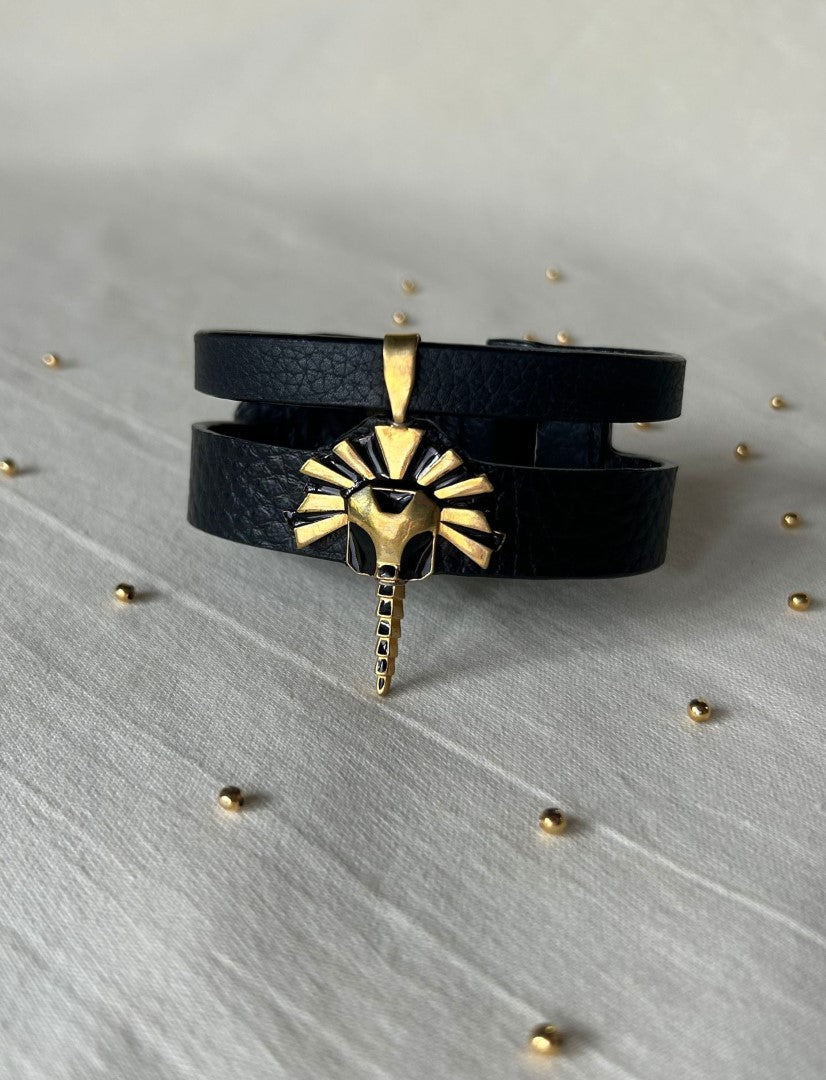 Timeless black leather wrap bracelet with gold lion head pendant on light fabric surface with small gold beads
