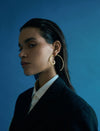 Profile of a woman wearing large gold spiral hoop earrings against a plain blue background
