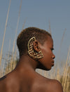Profile of a woman with short hair wearing large geometric gold earrings outdoors with tall grass and clear blue sky