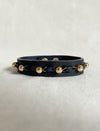 Black leather unisex bracelet with gold beads and braided gold thread on white fabric