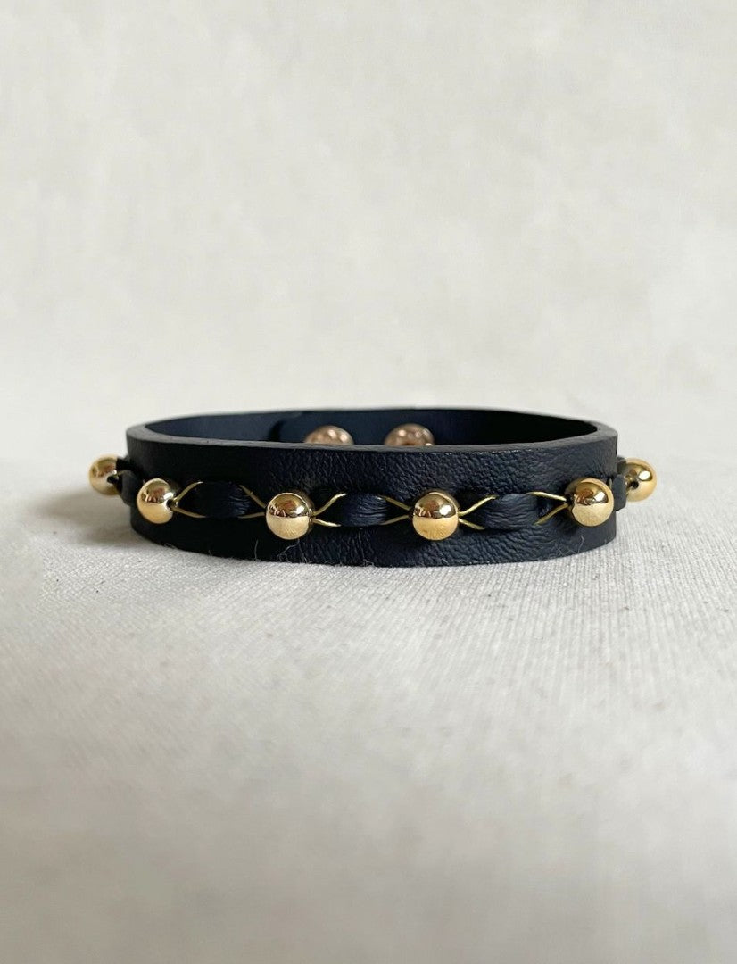Black leather unisex bracelet with gold beads and braided gold thread on white fabric