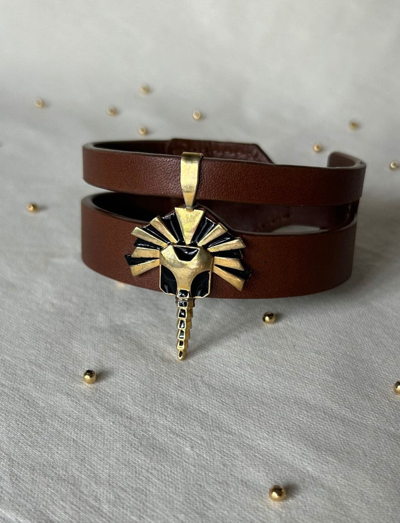 Timeless tan leather upcycled bracelet with gold and black tribal sun pendant on white fabric background