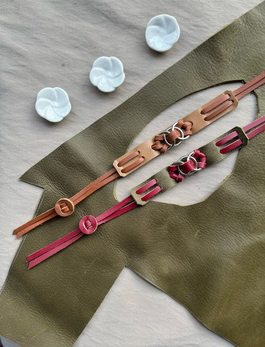 Handcrafted leather bracelets with intricate metal ring details on olive green leather backdrop and white ceramic flower beads