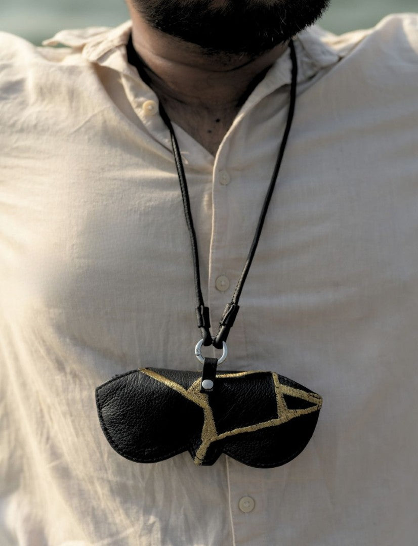 Man wearing beige shirt with black leather sunglasses pouch necklace featuring gold geometric design