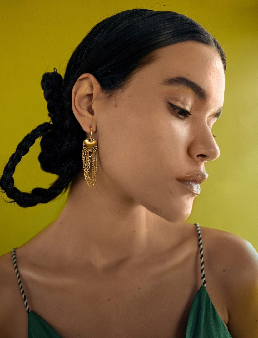 Close-up of woman with braided hair wearing gold chain earrings against yellow background