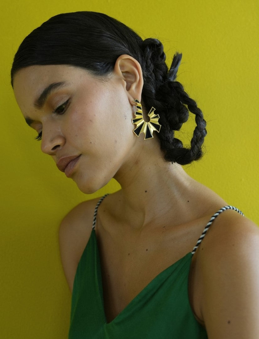 Woman wearing green dress and black enamel gold earrings with spiral design against yellow background