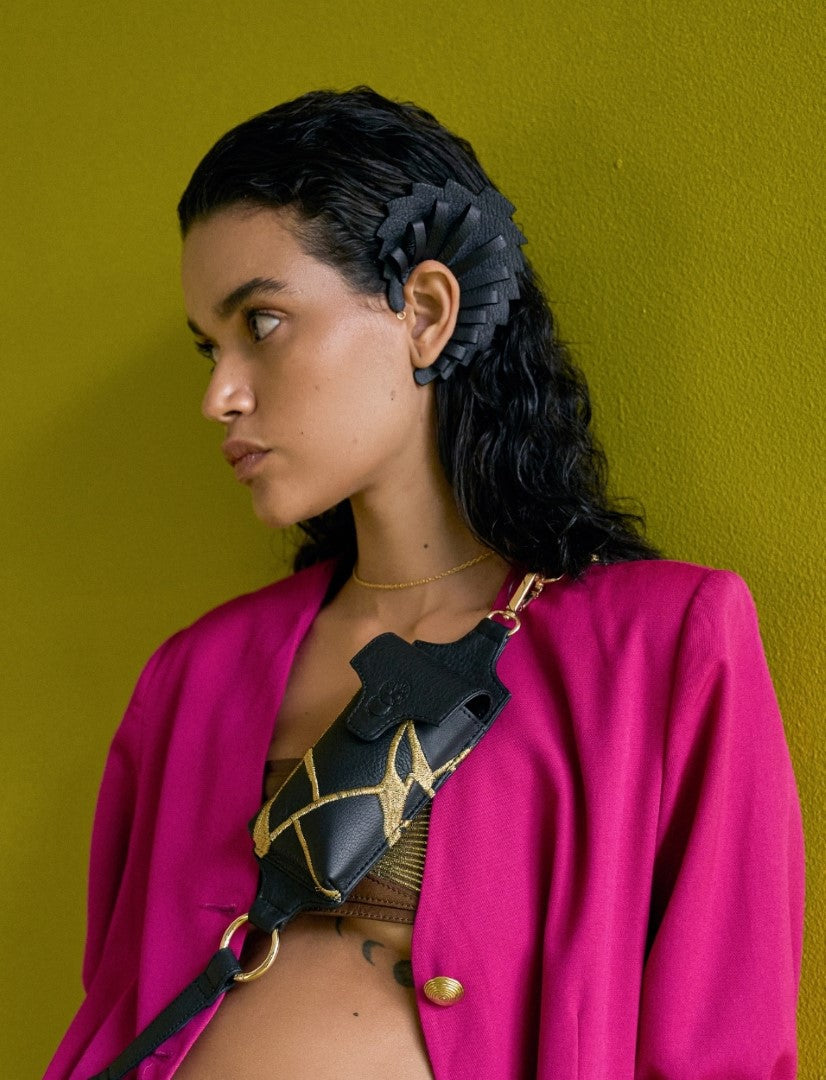 Woman wearing black leather upcycled ear cuff and black leather bag with gold embroidery, fuchsia blazer, green background