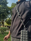 Person wearing black ribbed sweater with black padded leather phone sling bag in sunny outdoor park