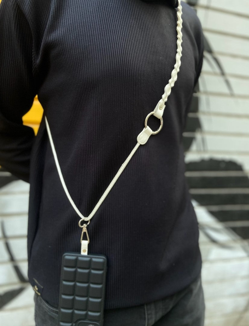 Person wearing a black sweater with a white braided leather phone sling holding a black textured phone case