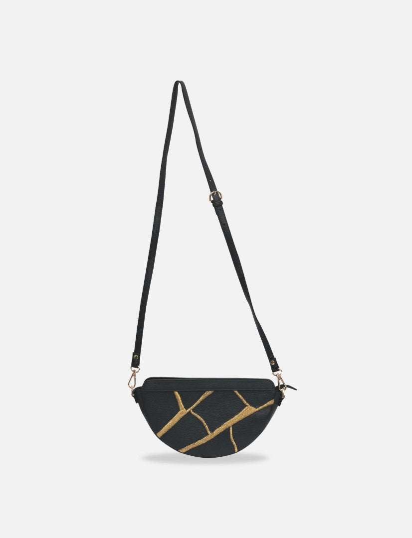 Black half-moon sling bag with gold crackle pattern and adjustable shoulder strap on white background
