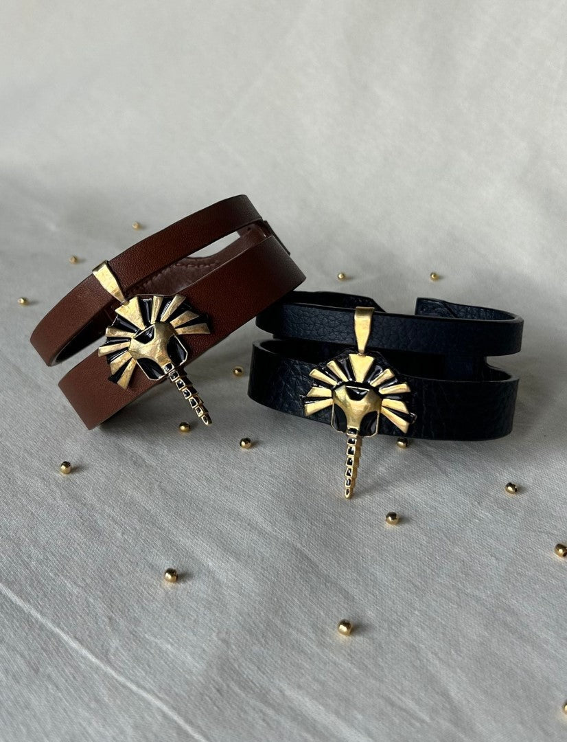 Handcrafted upcycled leather bracelets in brown and black with gold lion head charms displayed on fabric surface with small gold beads