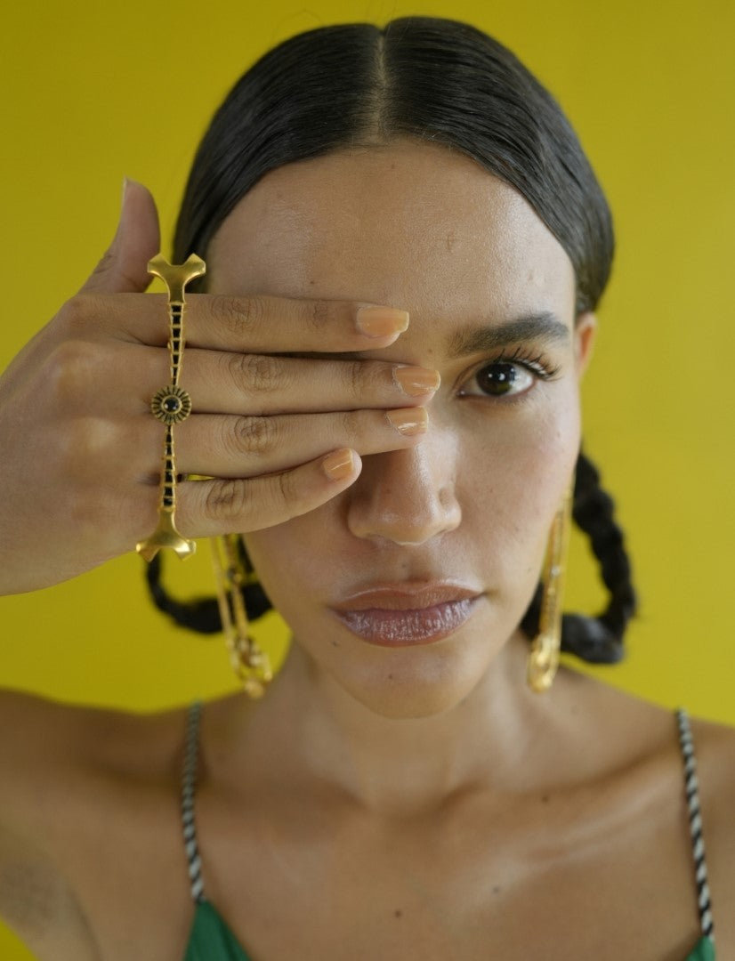 Close-up portrait of woman with braided hair wearing metallic multifinger ring and gold earrings against yellow background