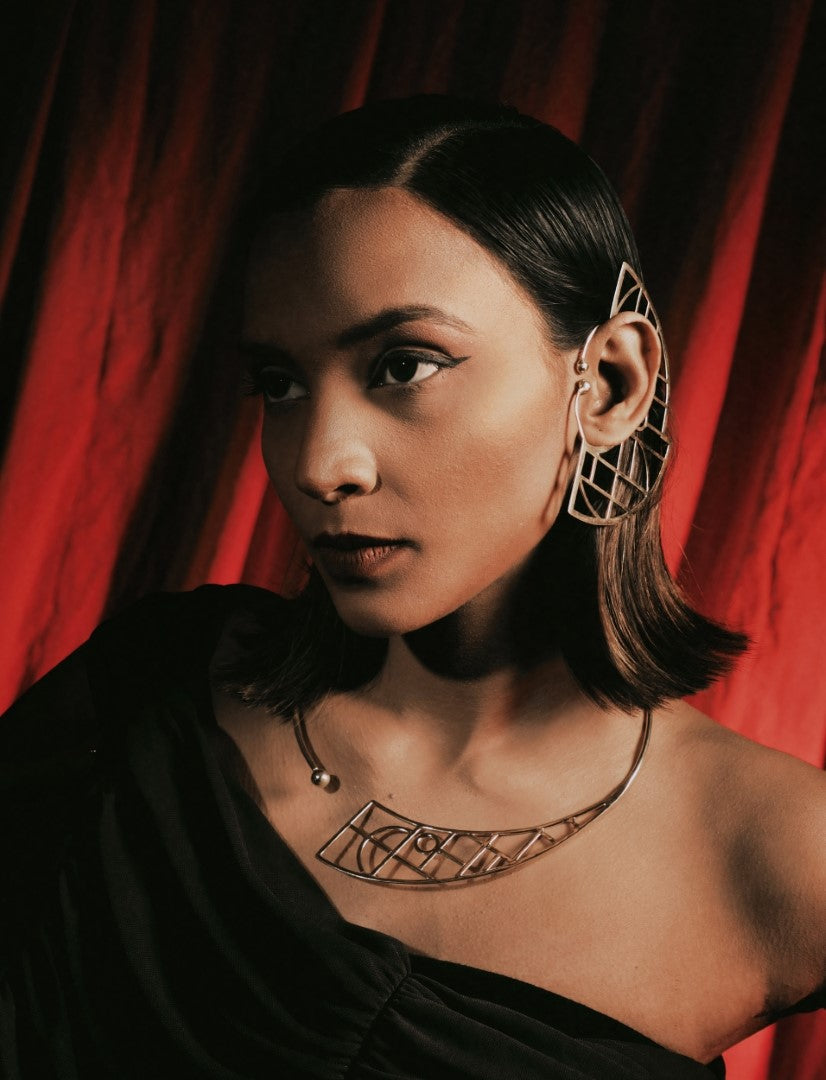 Portrait of woman wearing geometric metal ear cuff and matching necklace against red curtain backdrop